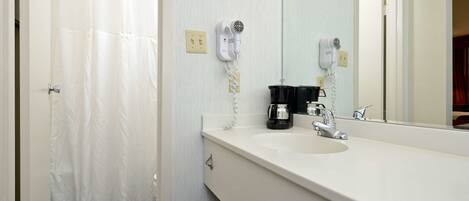 A bathroom with a white sink, a mirror, a hairdryer, and a shower curtain.
