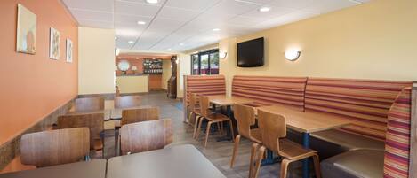 A restaurant with booths and tables, wooden chairs, a clock, and a TV on the wall.