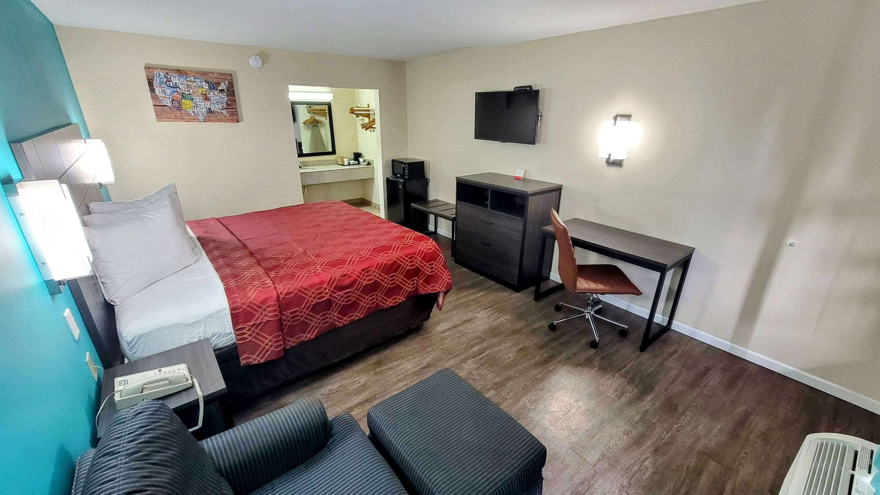 A hotel room with a bed, a desk, a chair, a small couch, a TV, and a mirror.