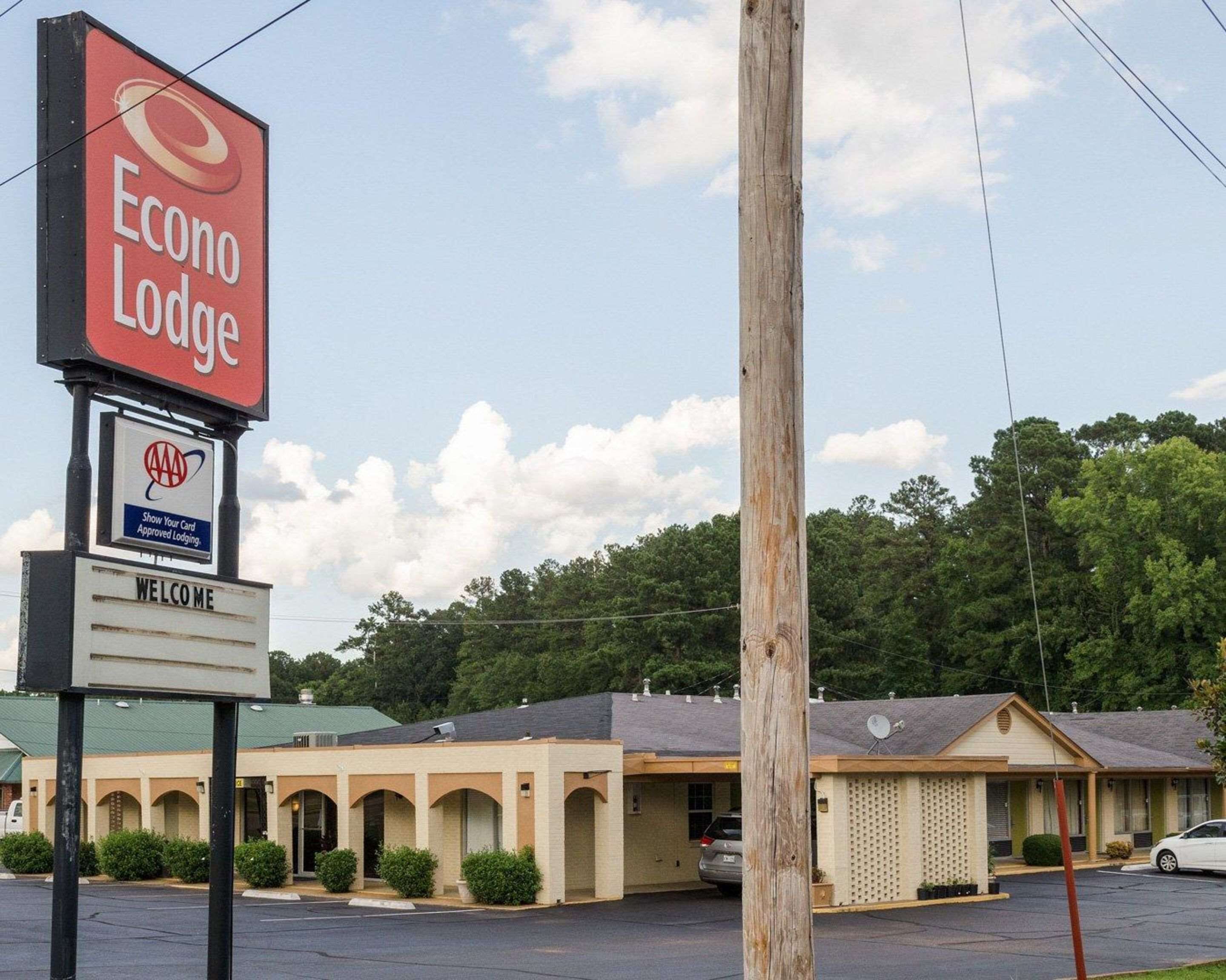 A motel named Econo Lodge with a signboard, a 'Show Your Card' AAA Approved Lodging sign, and a 'Welcome' sign.