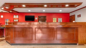 Una recepción con encimera de madera, pared roja, televisor de pantalla plana y puerta con un cartel en la parte superior.
