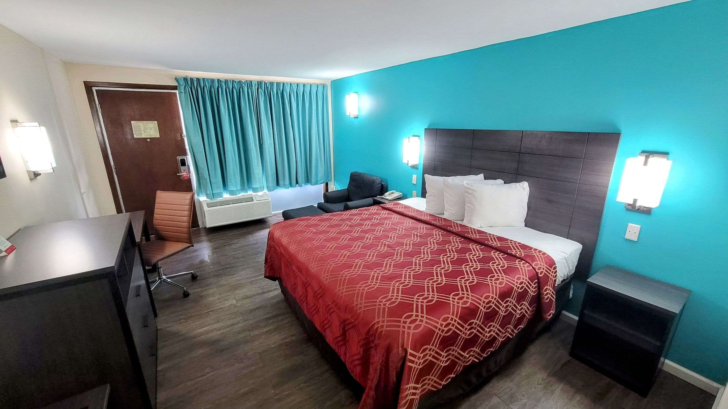 A hotel room with a bed, desk, chair, and a window with curtains.