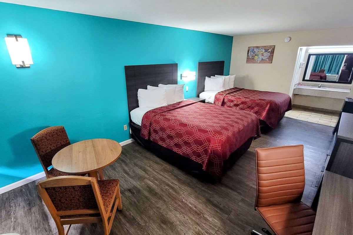 A hotel room with two beds, a small round table, a chair, and a kitchenette.