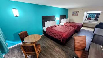 A hotel room with two beds, a small round table, a chair, and a kitchenette.