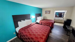 Habitación de hotel con dos camas, paredes verde azulado, piso de madera, un escritorio pequeño y un baño con espejo y lavamanos.