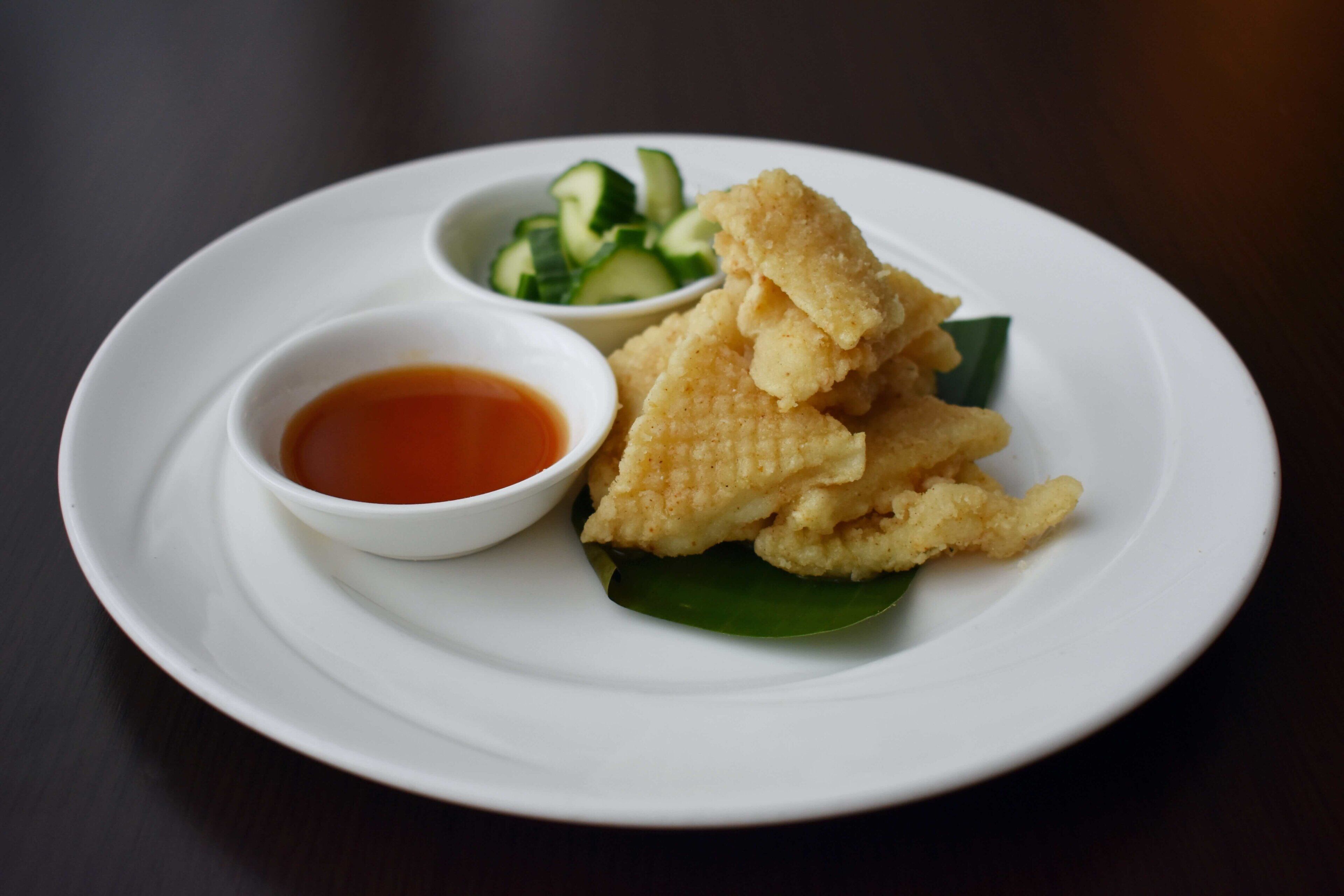 A plate with fried items, a small bowl of sauce, and a bowl of sliced cucumbers.