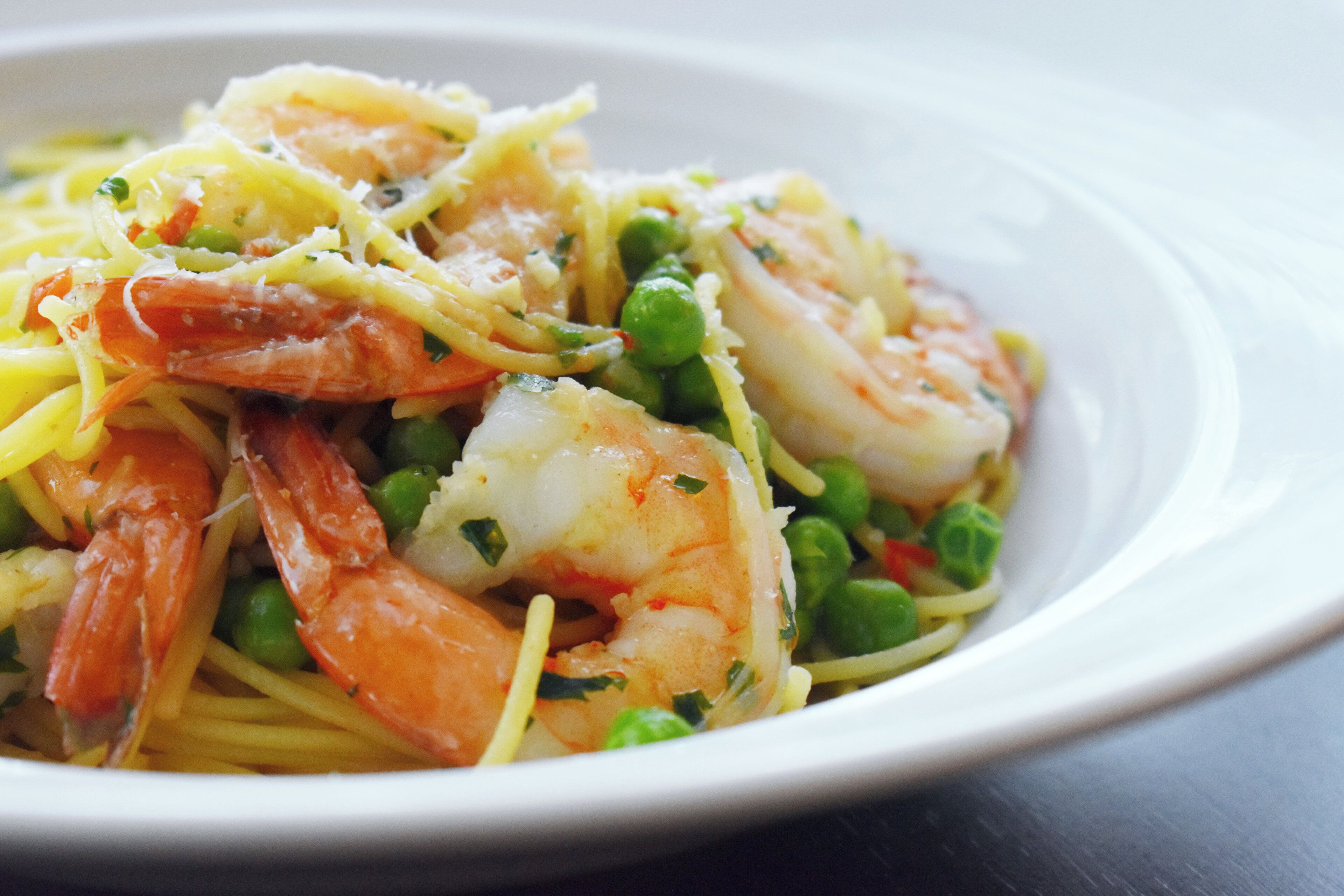 Un plato de pasta con camarones, guisantes y queso.
