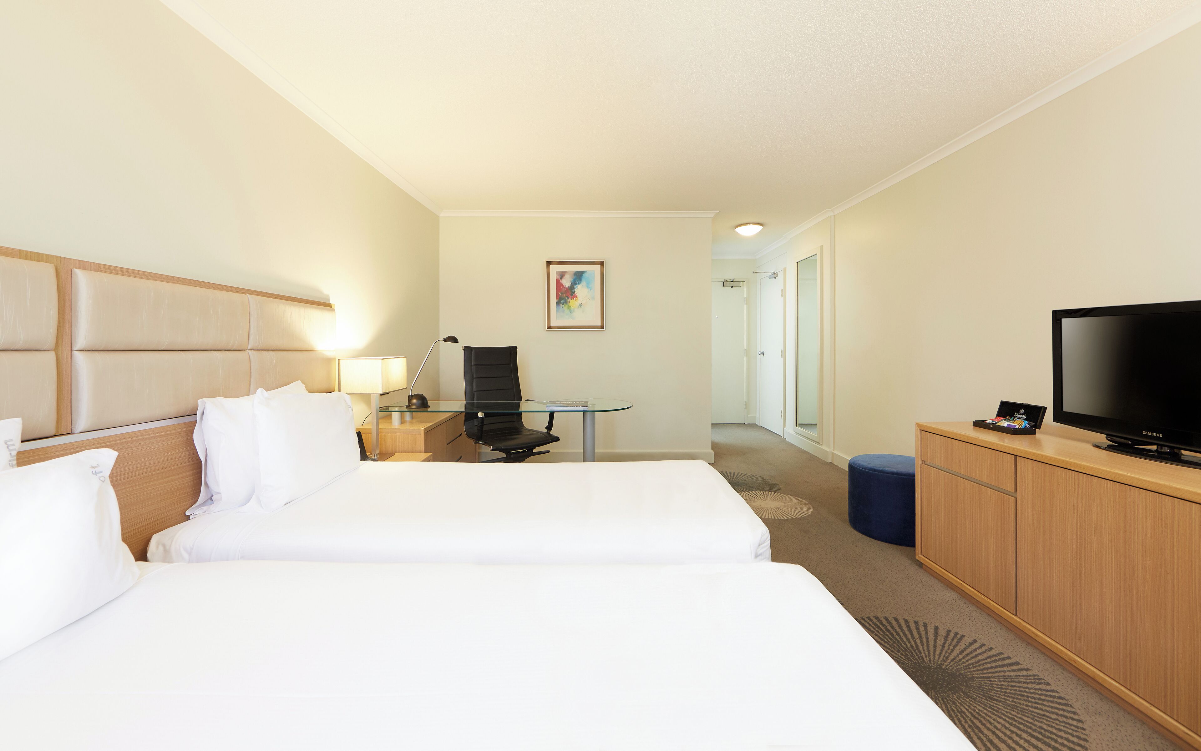 Une chambre d’hôtel avec deux lits, un bureau avec une chaise, une télévision et une petite table avec une lampe.
