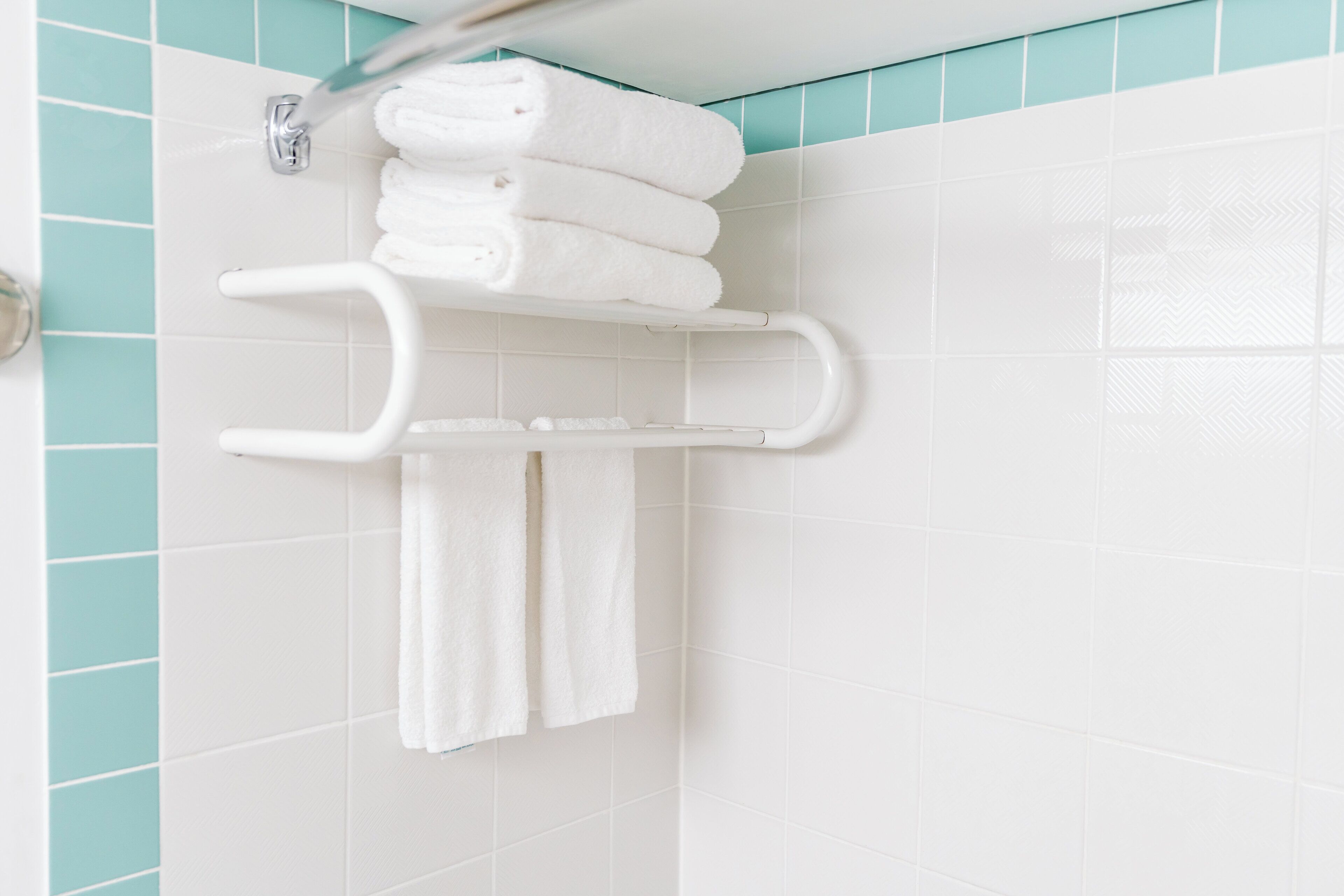 Une salle de bain avec des carreaux blancs, un porte-serviettes blanc et une serviette blanche suspendue.