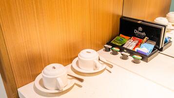 A coffee station with two white cups and saucers, a tray with coffee packets, and a branded box.