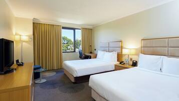 A hotel room with two beds, a desk with a TV, and a window with curtains.