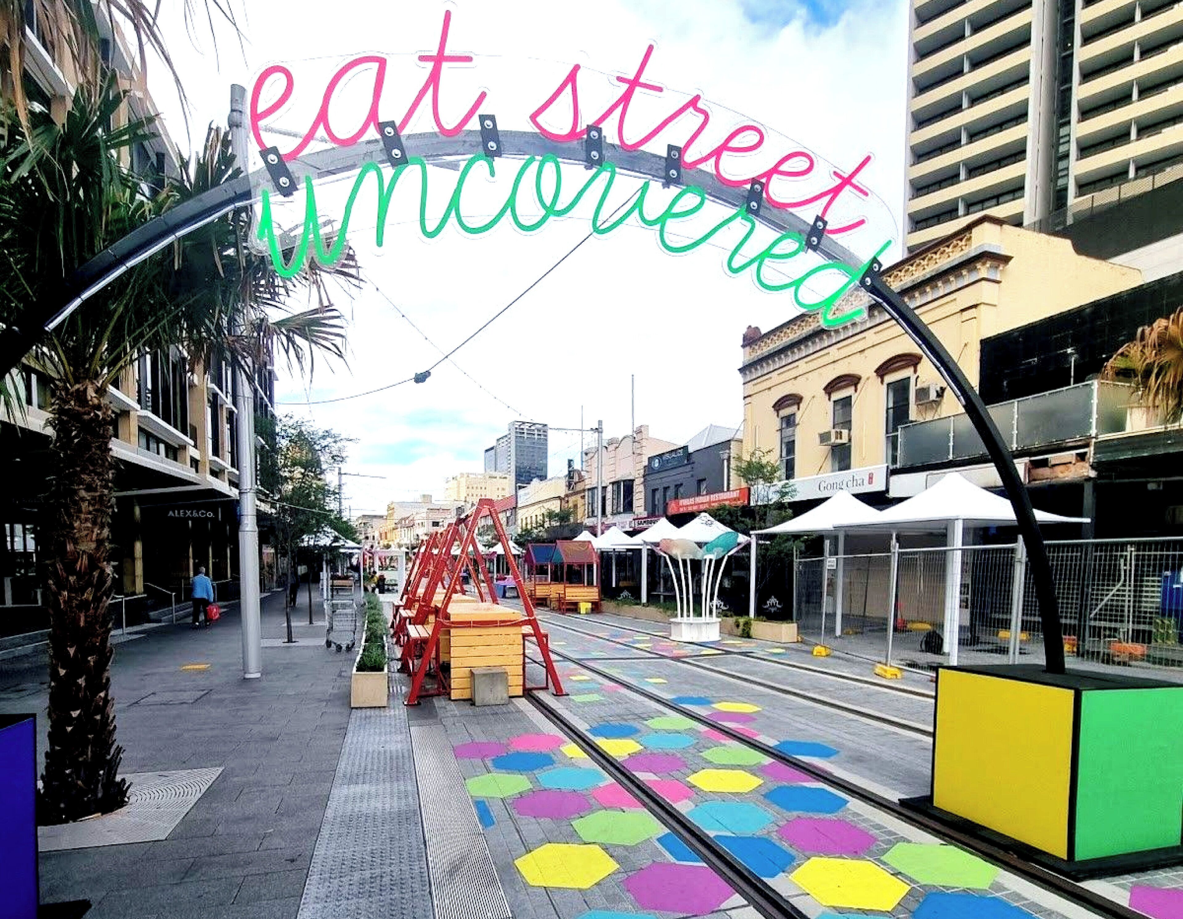 A street with colorful hexagonal tiles, a red swing set, and a sign that reads "eat street uncensored".