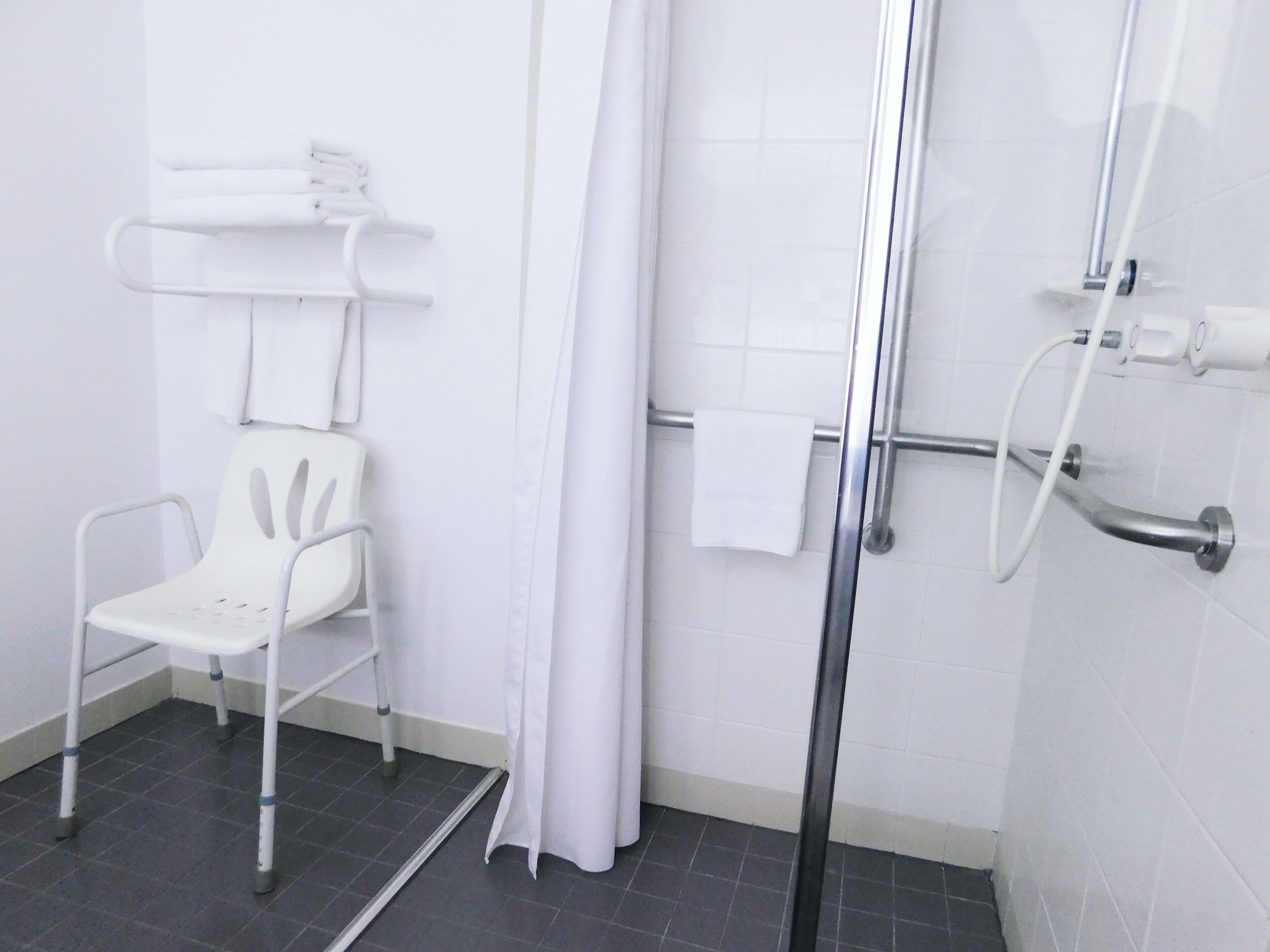A bathroom with a shower, a white chair, and a towel rack.