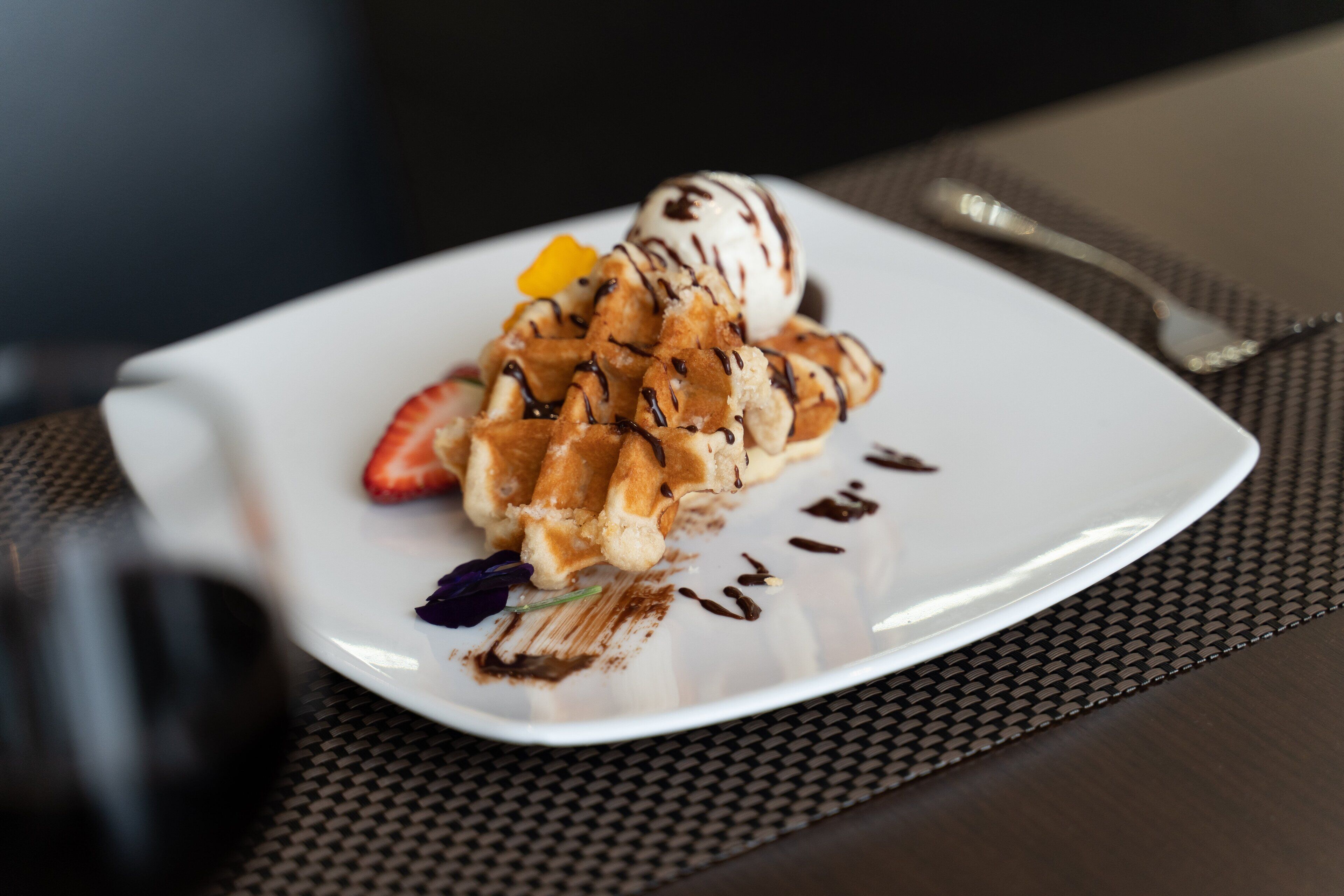 A plate of waffles with chocolate drizzle and a scoop of ice cream.