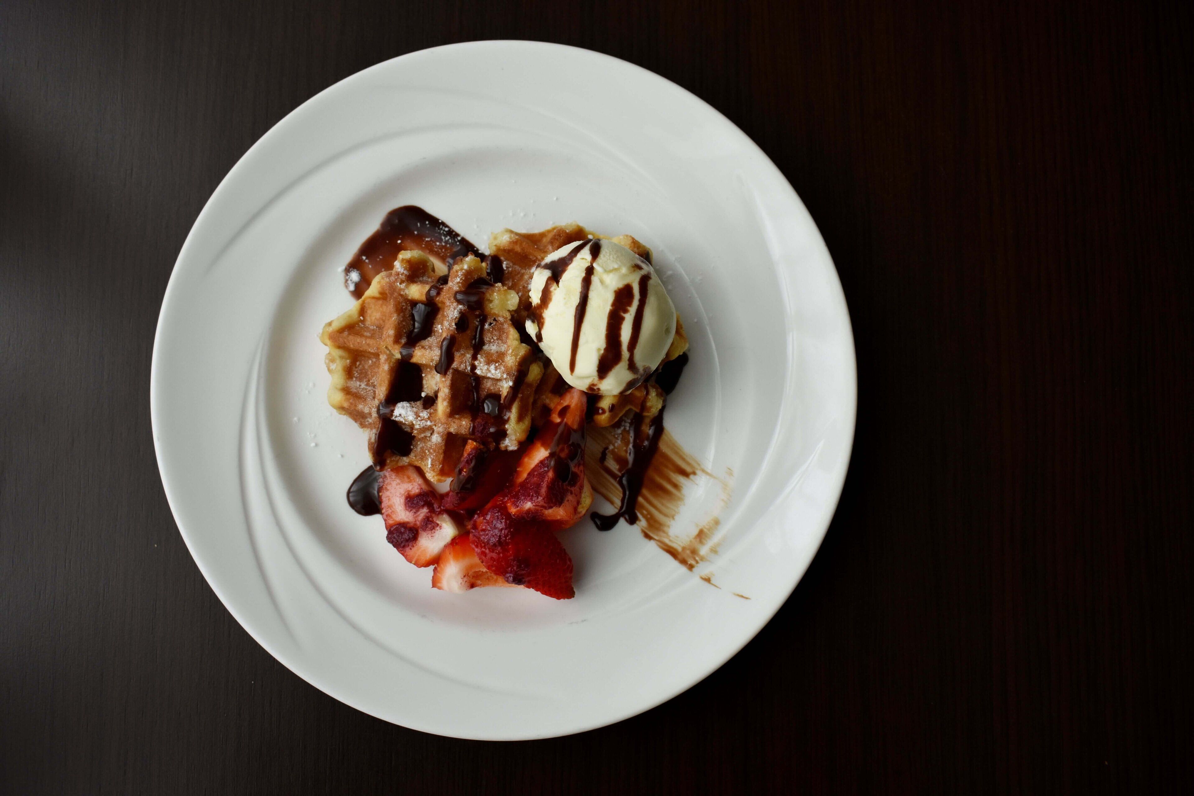 A dessert plate with a waffle, ice cream, and strawberries on a white plate.