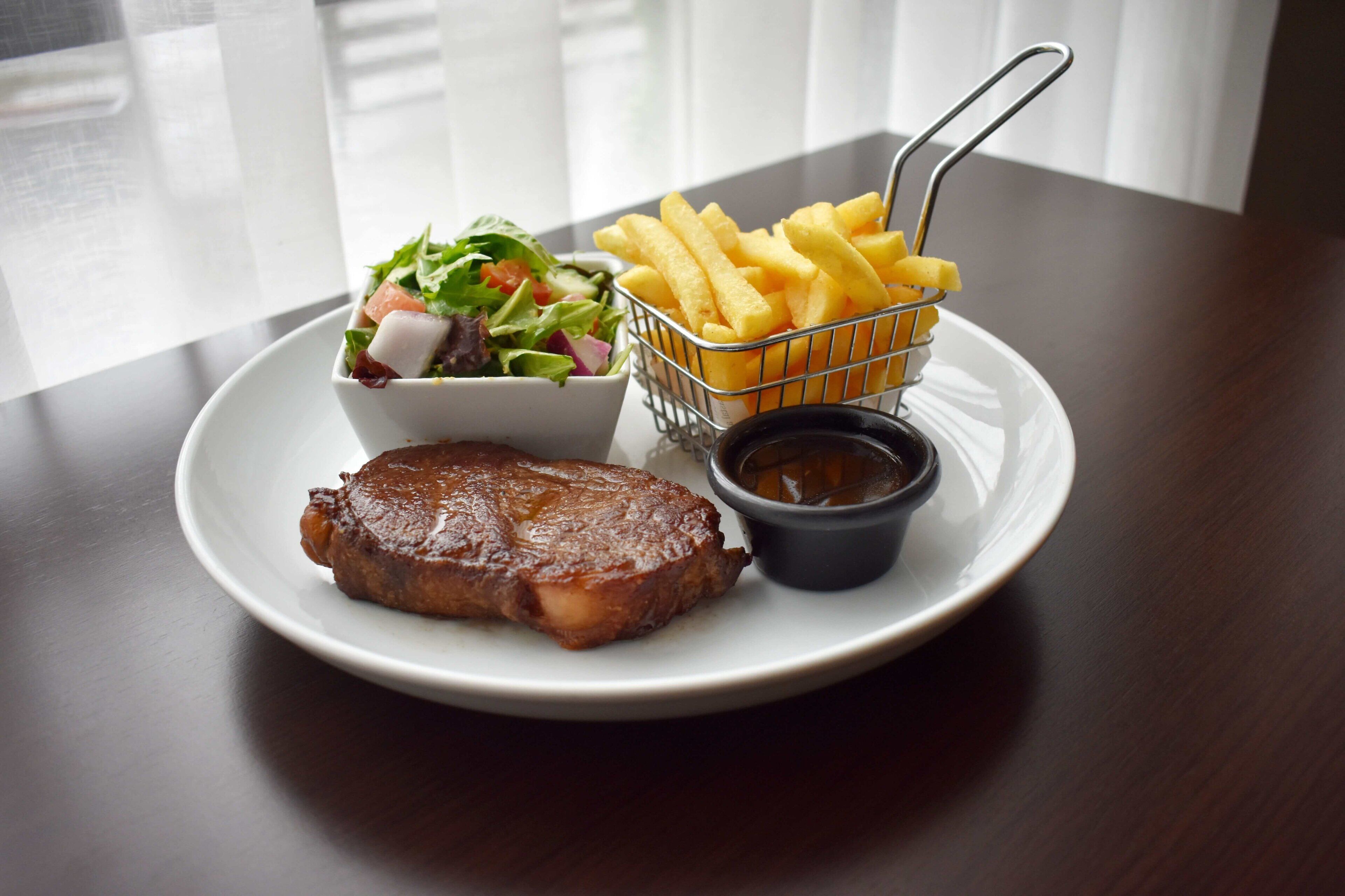 A plate with a steak, a side salad, French fries, and a small container of sauce.