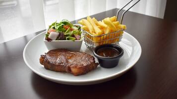 A plate with a steak, a side salad, French fries, and a small container of sauce.