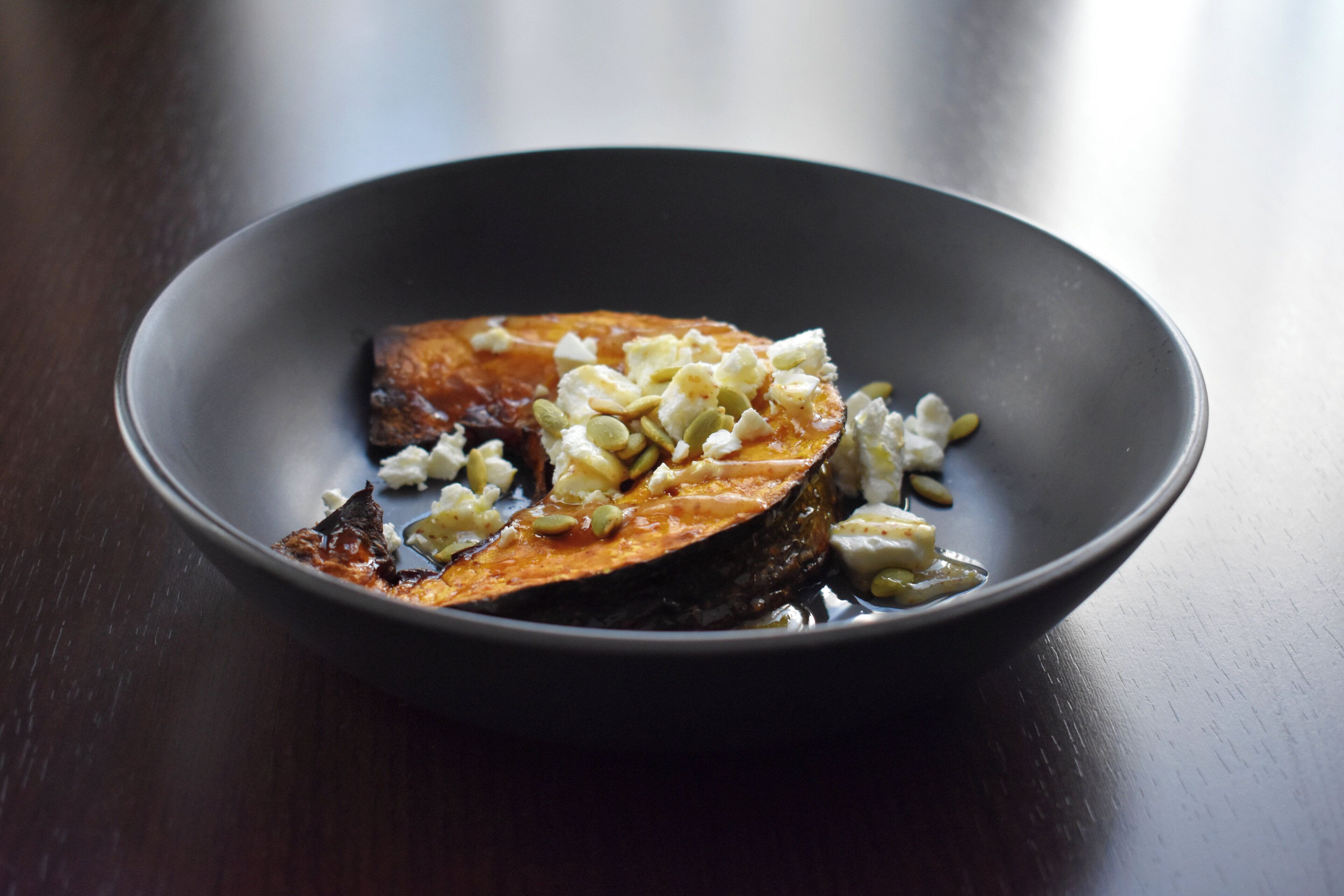 A dark-colored bowl containing a piece of salmon topped with a creamy sauce and chopped nuts.