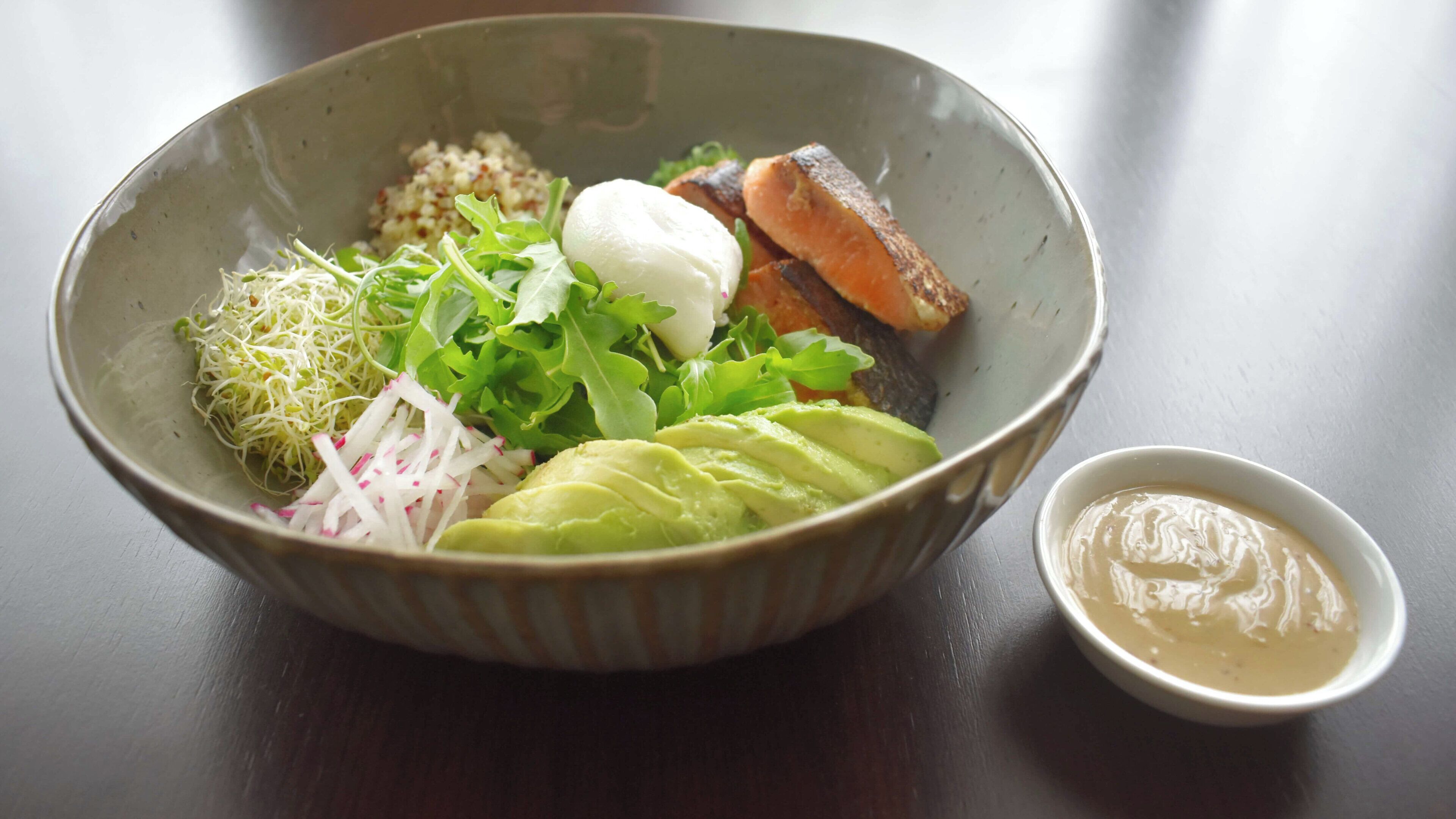 A bowl of food with various ingredients and a small bowl of sauce.