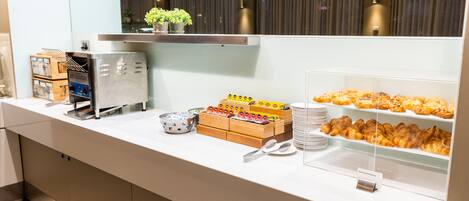 A buffet counter with various food items, including pastries and a coffee machine.