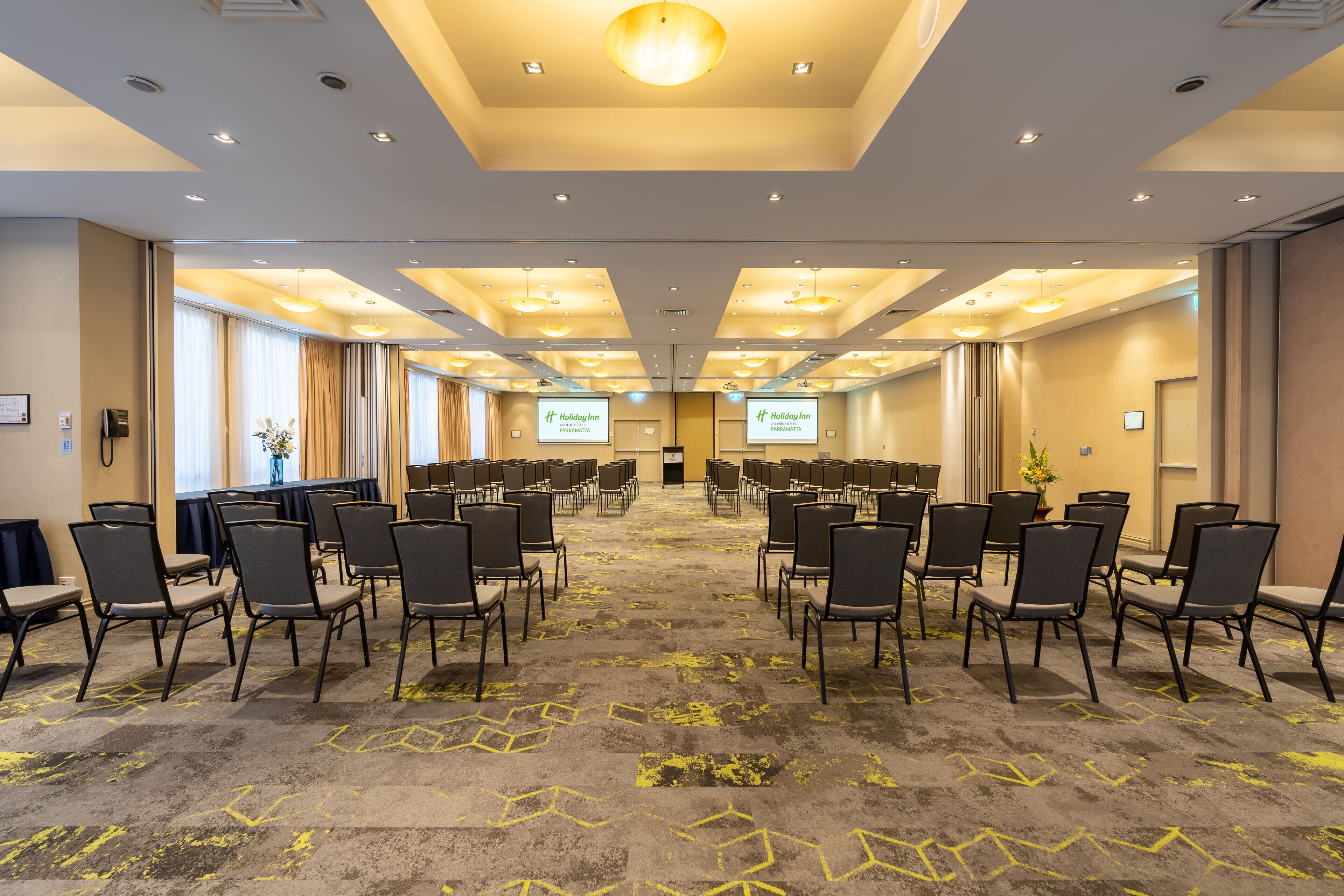Un salón de conferencias con filas de sillas, piso alfombrado e iluminación empotrada en el techo.