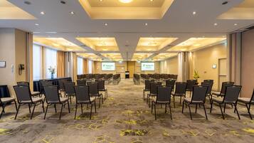 Un salón de conferencias con filas de sillas, piso alfombrado e iluminación empotrada en el techo.