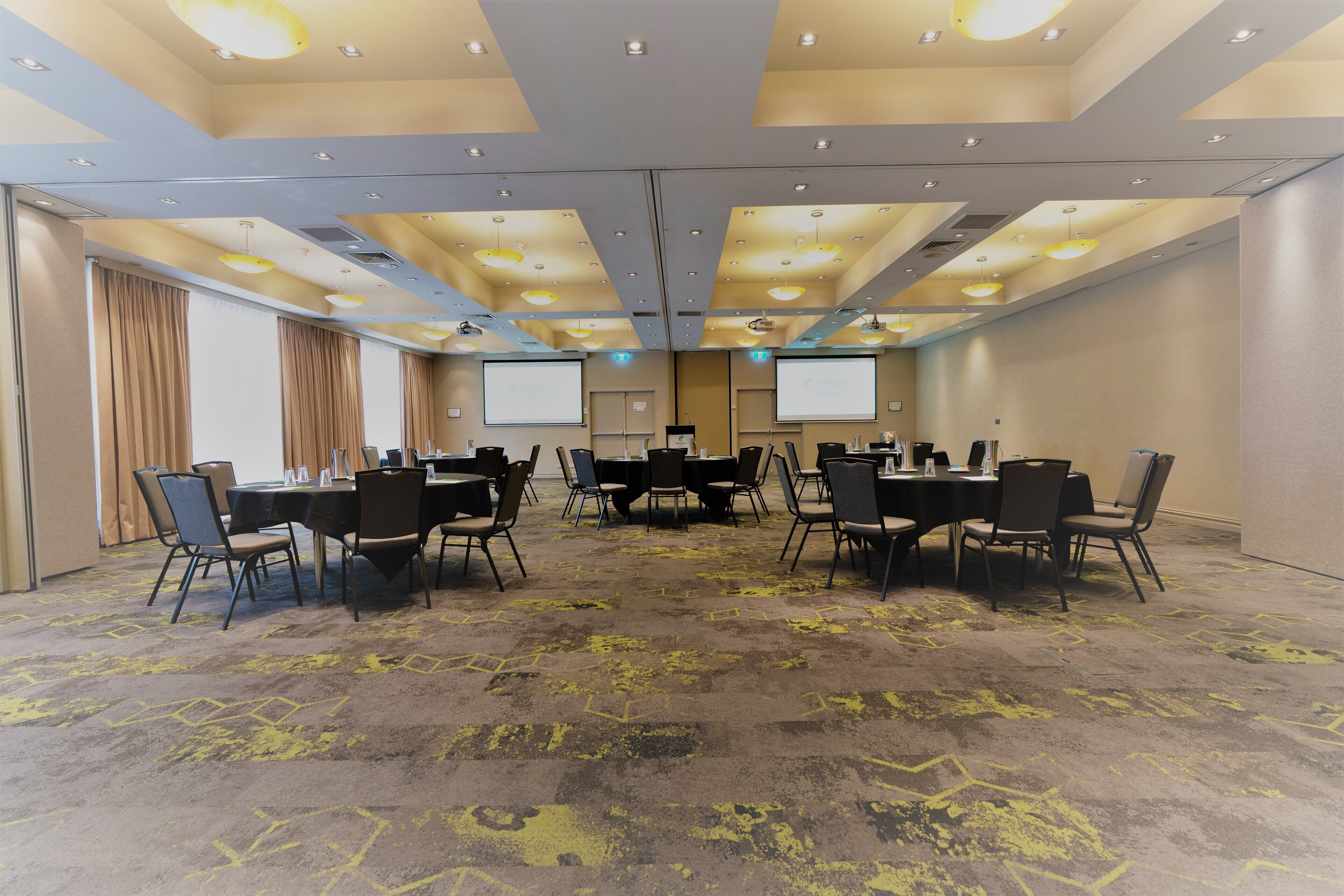 A conference room with a carpeted floor, tables, chairs, and a projector screen.