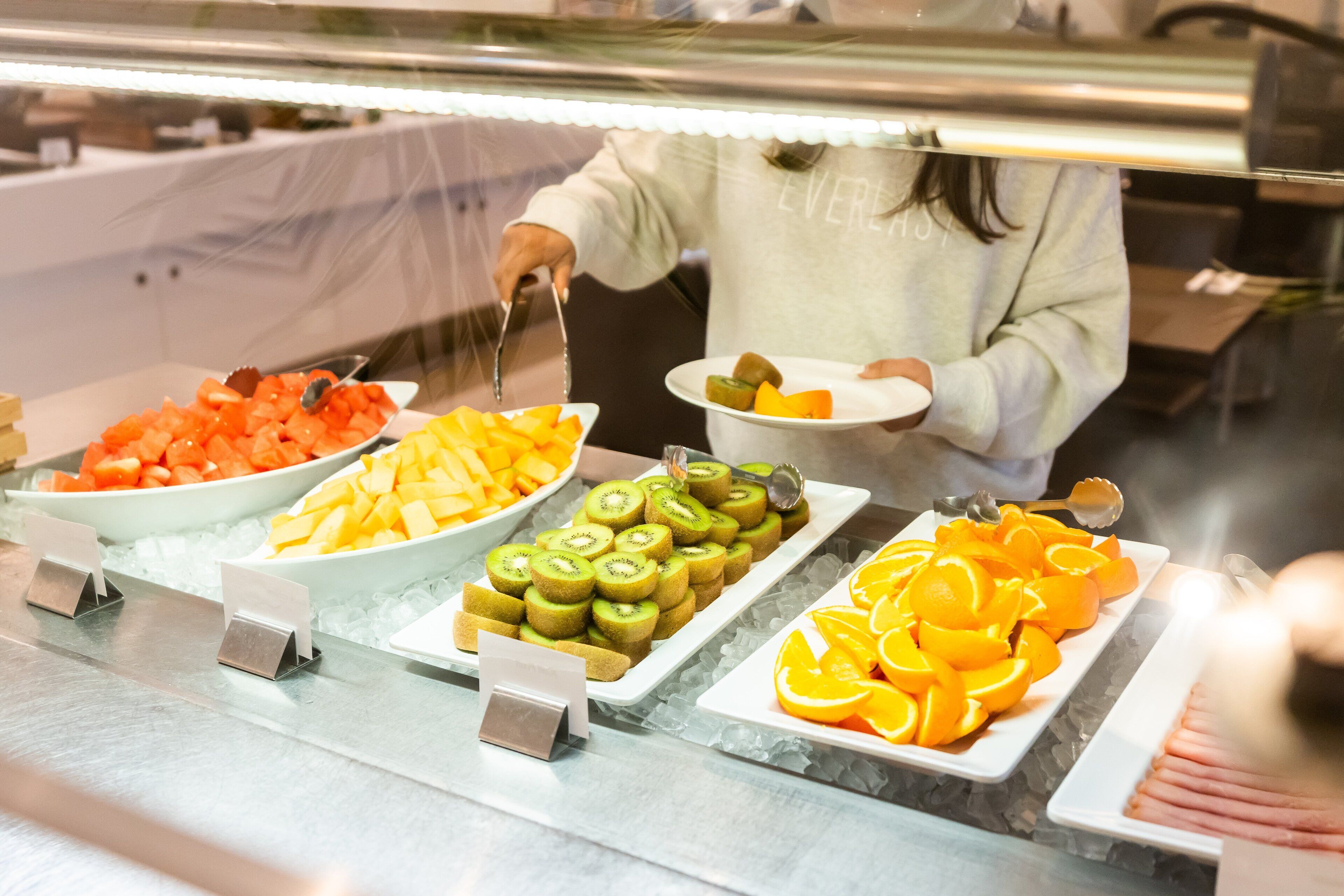 A buffet with various fruits and a person serving.