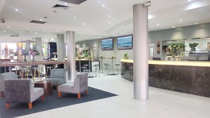Een moderne hotellobby met een receptiebalie, een zithoek en grote ramen.