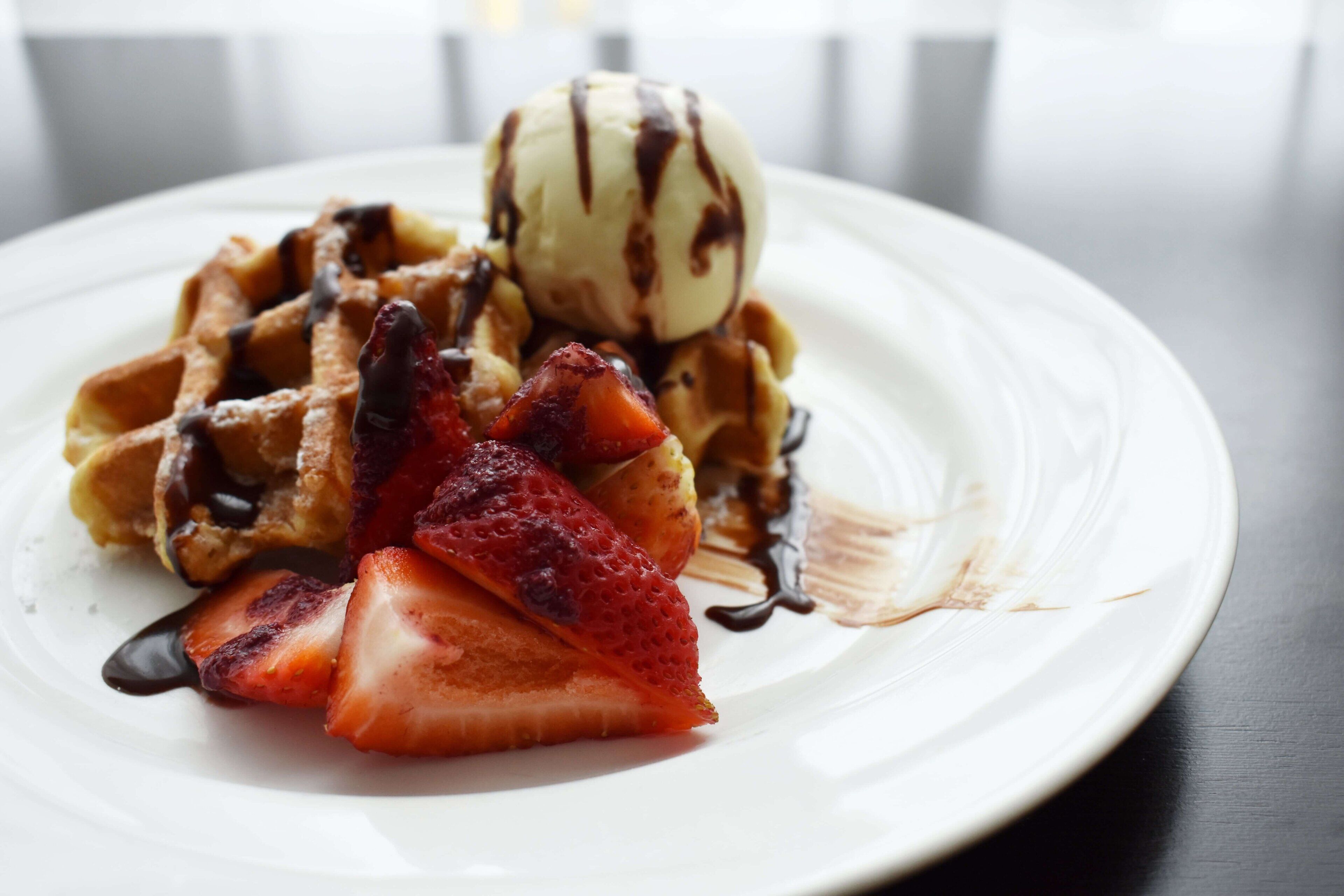 Un piatto con waffle, fragole e una pallina di gelato.