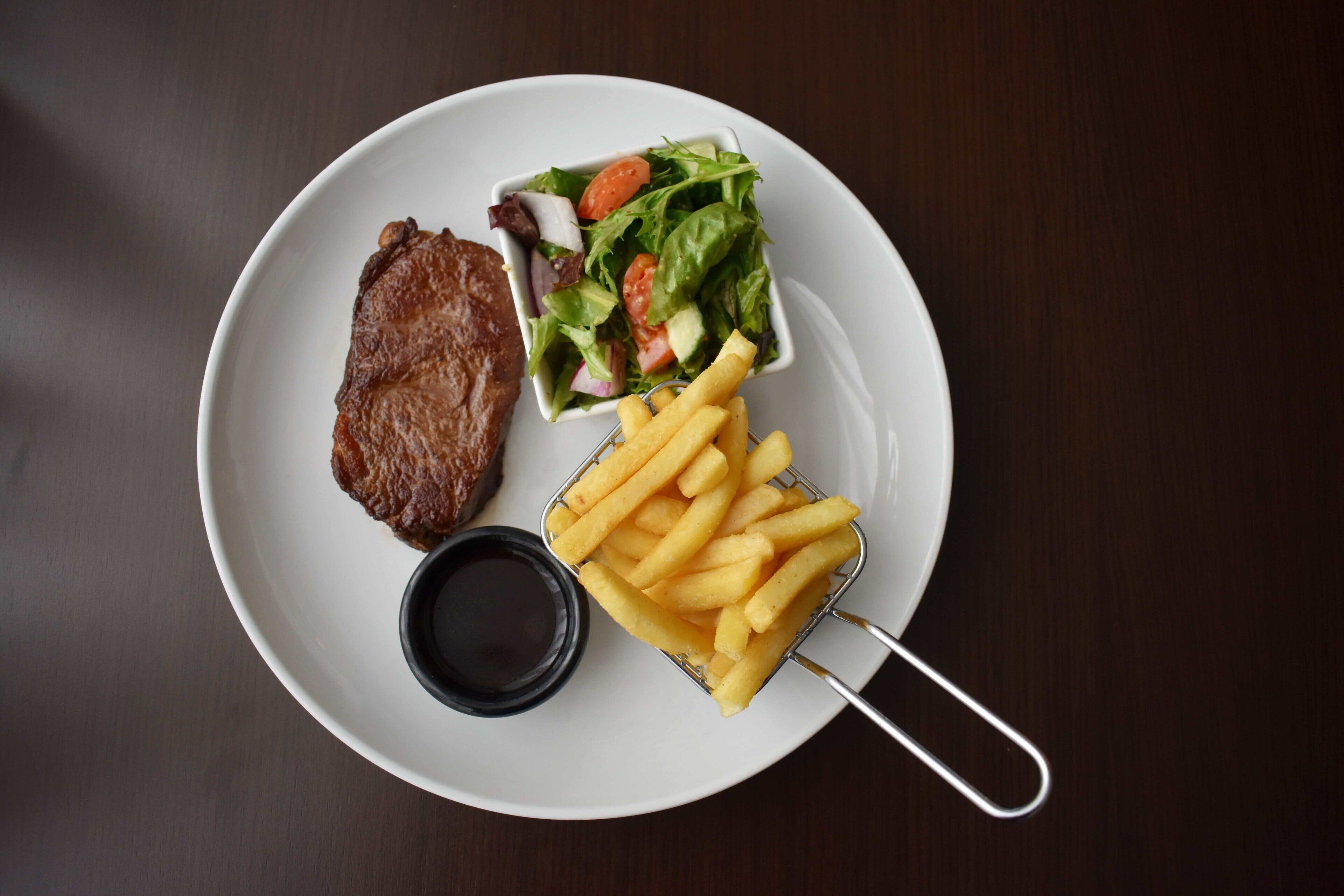 A plate with a steak, a small salad, and French fries.