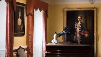 A room with a large portrait, a piano, and a chandelier.