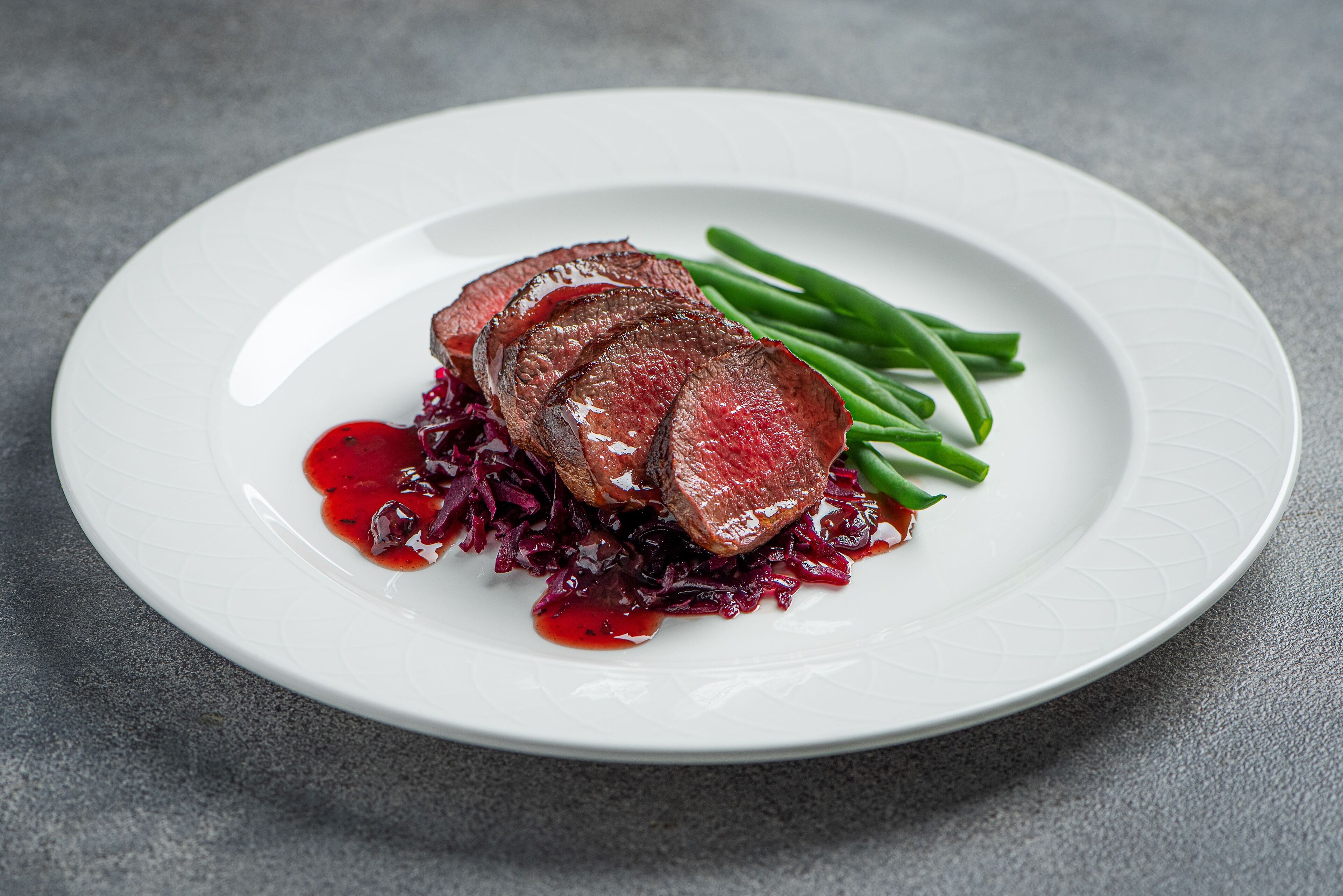 Um prato com carne fatiada, vagem e repolho roxo.