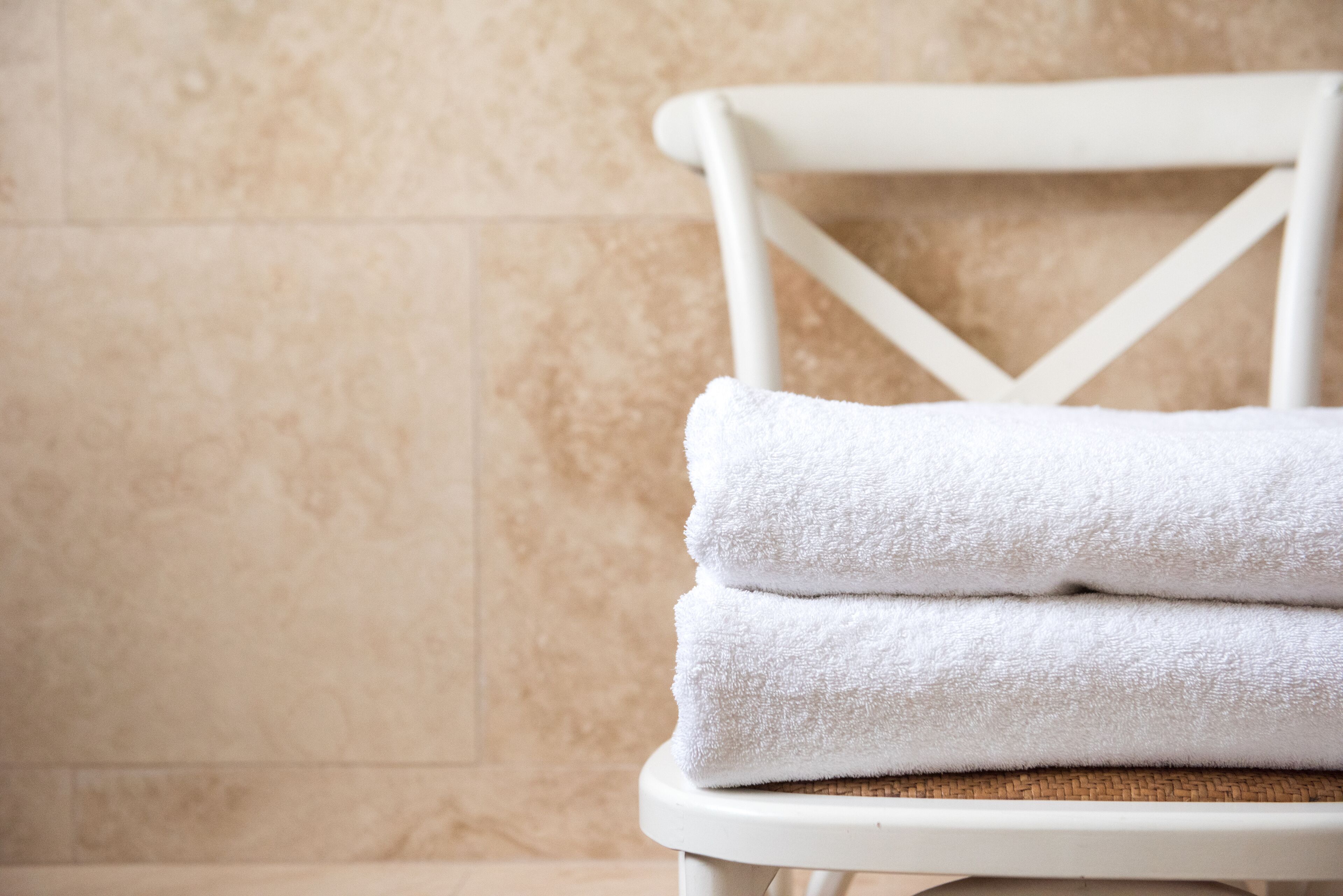 A stack of white towels on a white chair against a beige tiled wall.