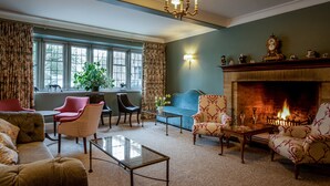Un salon chaleureux avec une cheminée, des fauteuils confortables et de grandes fenêtres.