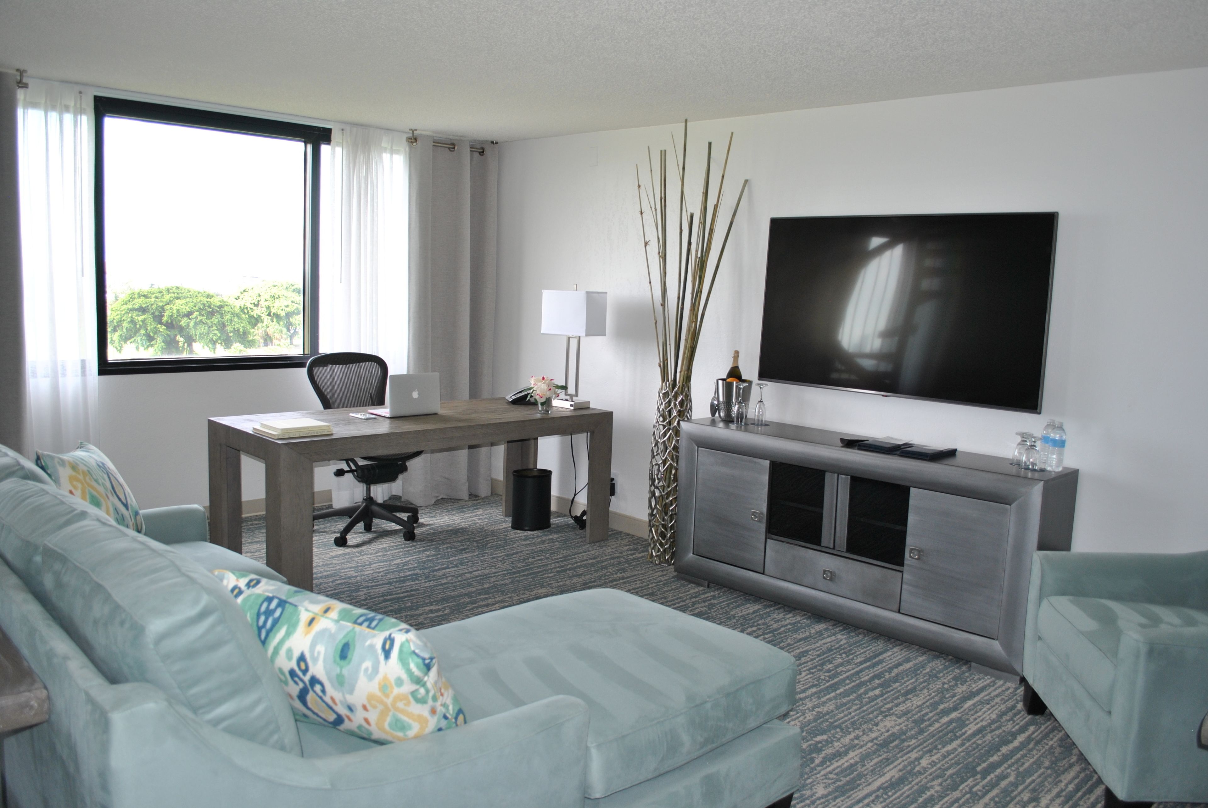 Habitación de hotel moderna con un ventanal grande, un escritorio, un sofá cómodo, un televisor de pantalla plana y una decoración minimalista.