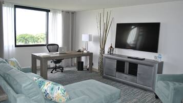 Habitación de hotel moderna con un ventanal grande, un escritorio, un sofá cómodo, un televisor de pantalla plana y una decoración minimalista.