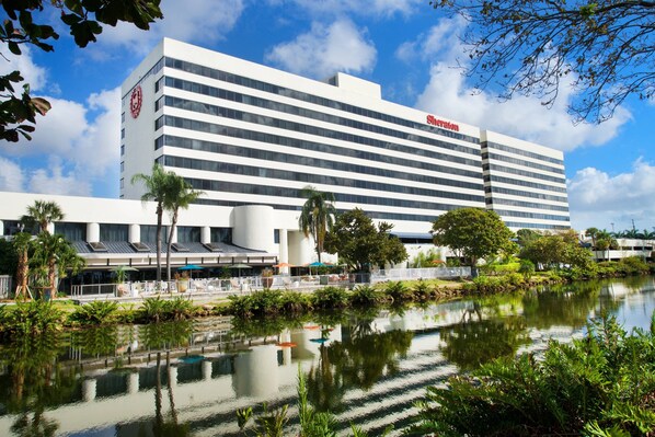 Un hotel moderno con una grande piscina specchiante, palme e un cielo azzurro limpido.