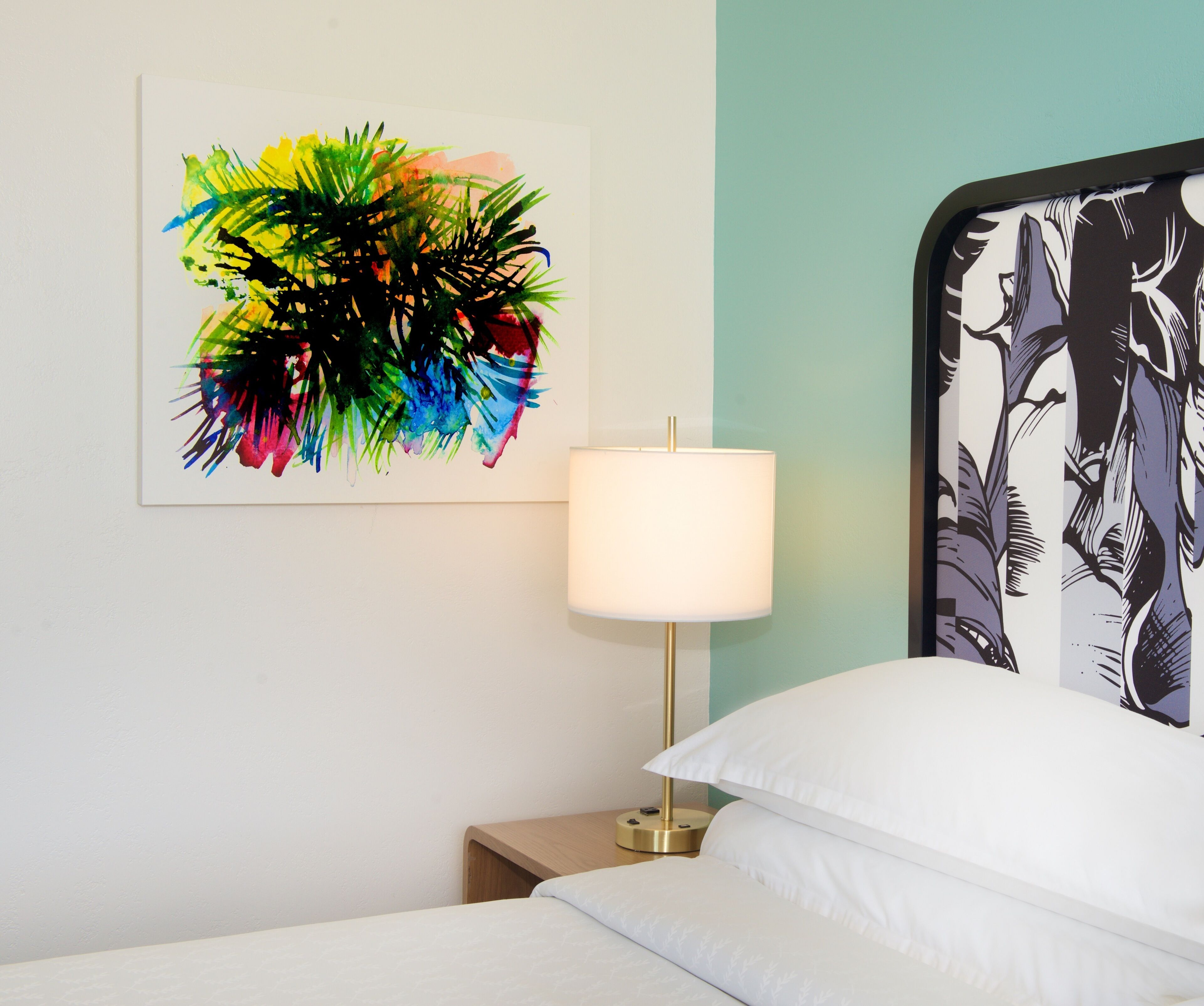 Une chambre d’hôtel avec un lit, une table de chevet avec une lampe et un tableau abstrait aux couleurs vives accroché au mur.