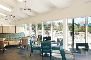 Un'ampia sala da pranzo interna con soffitto alto, grandi finestre e vista sul patio esterno.