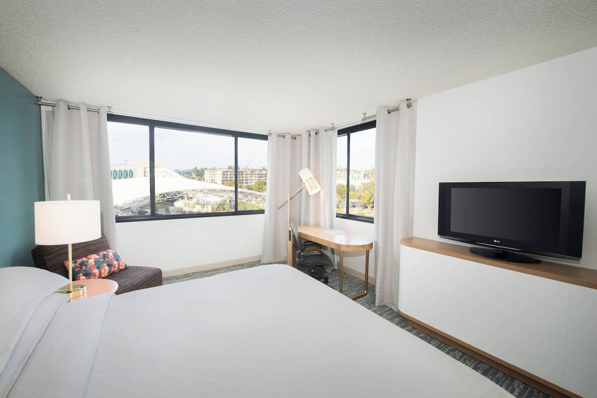 Habitación de hotel con cama, escritorio, televisión y vista a edificios fuera de la ventana.