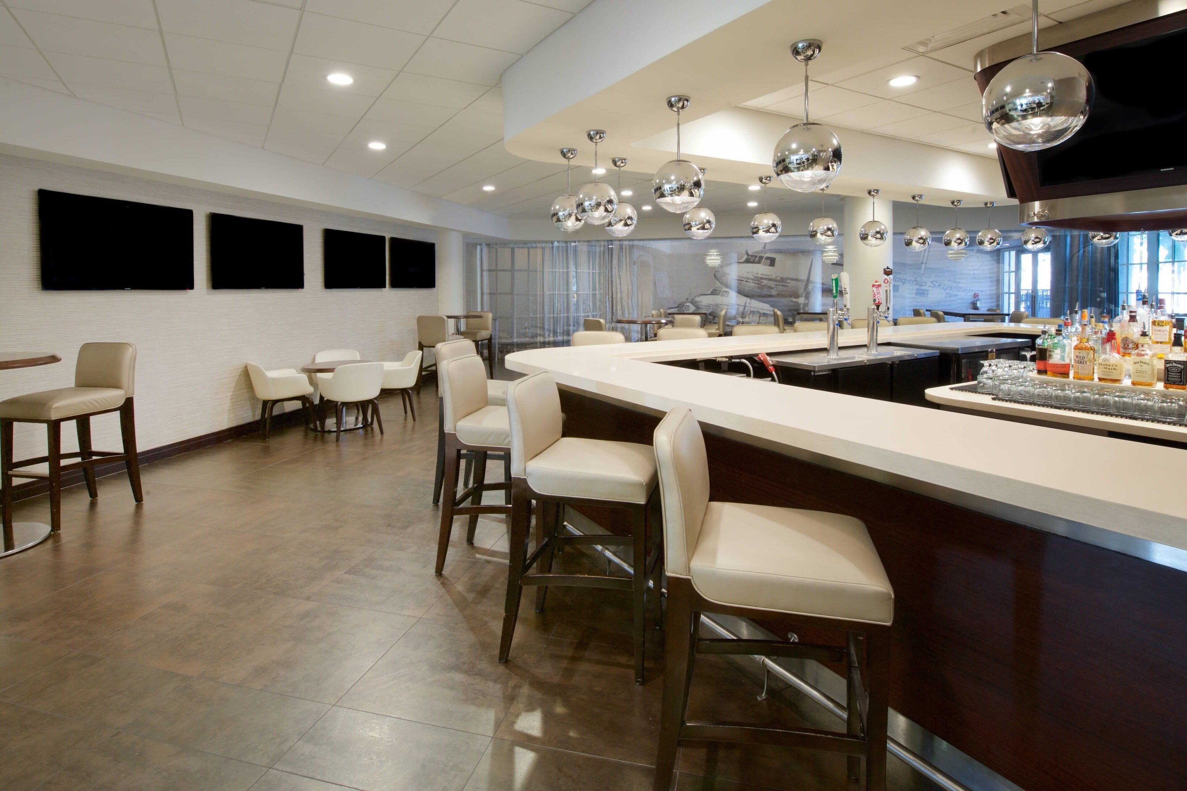 A modern bar area with a long counter, multiple bar stools, and a variety of bottles.
