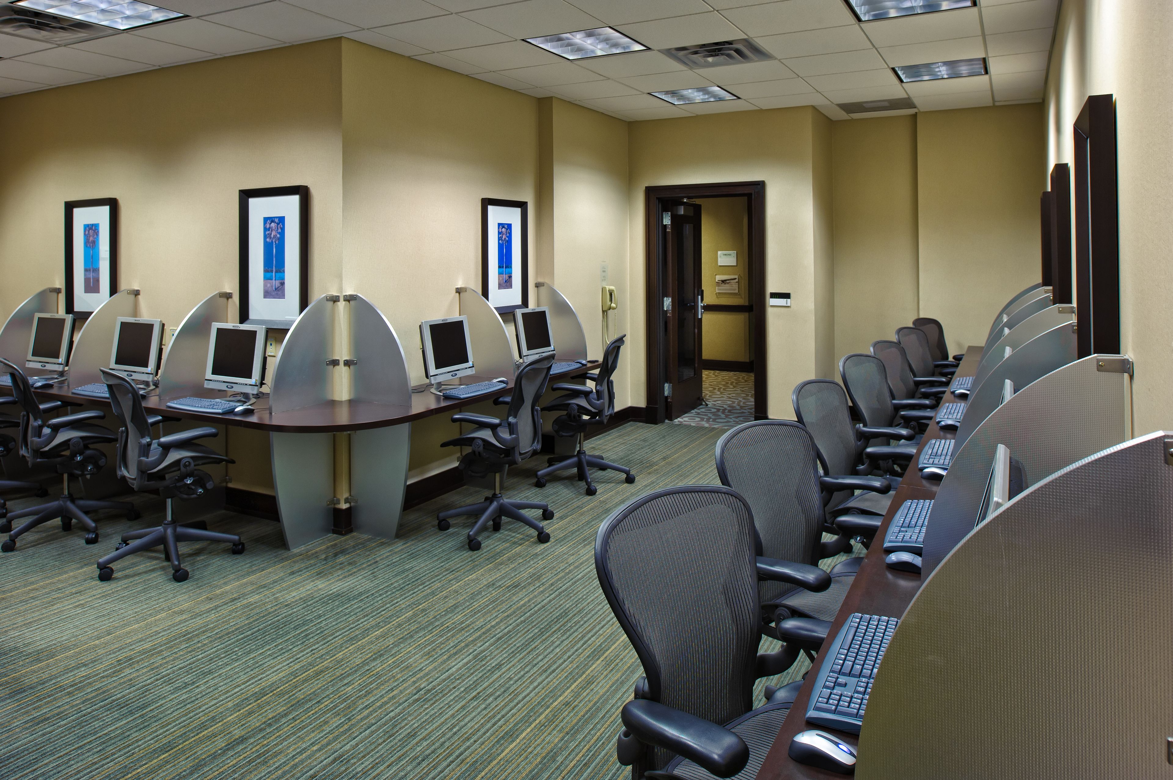 A conference room with multiple computer stations, ergonomic chairs, and a carpeted floor.