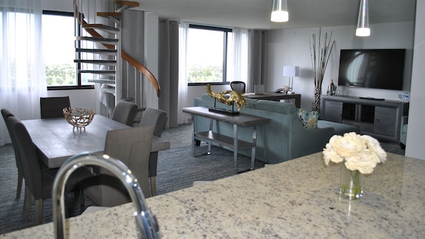 Een moderne hotelkamer met een zithoek, een woongedeelte met een bank en televisie, een trap en een groot raam.