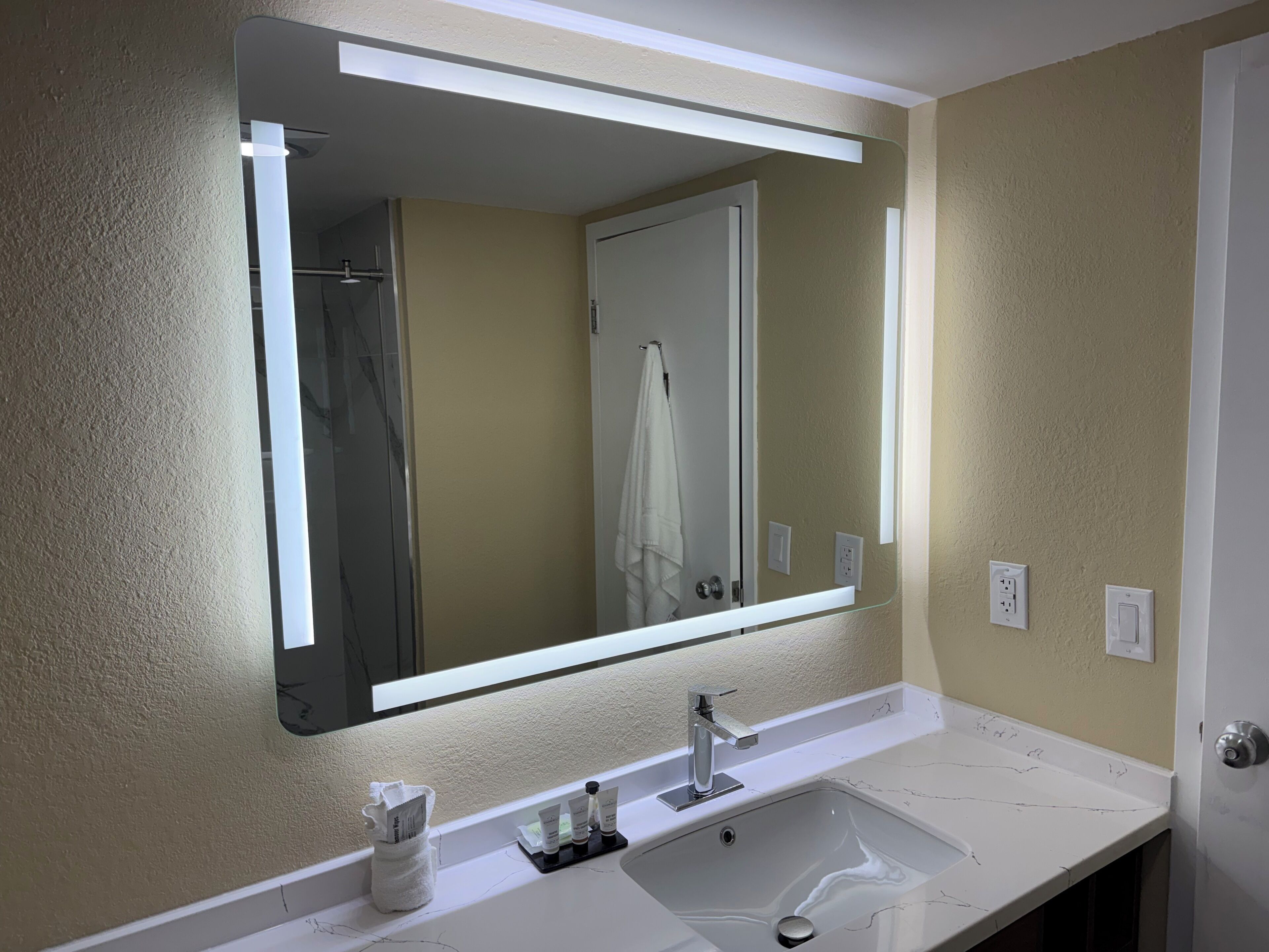 A bathroom with a large mirror, a white sink, and a towel rack.