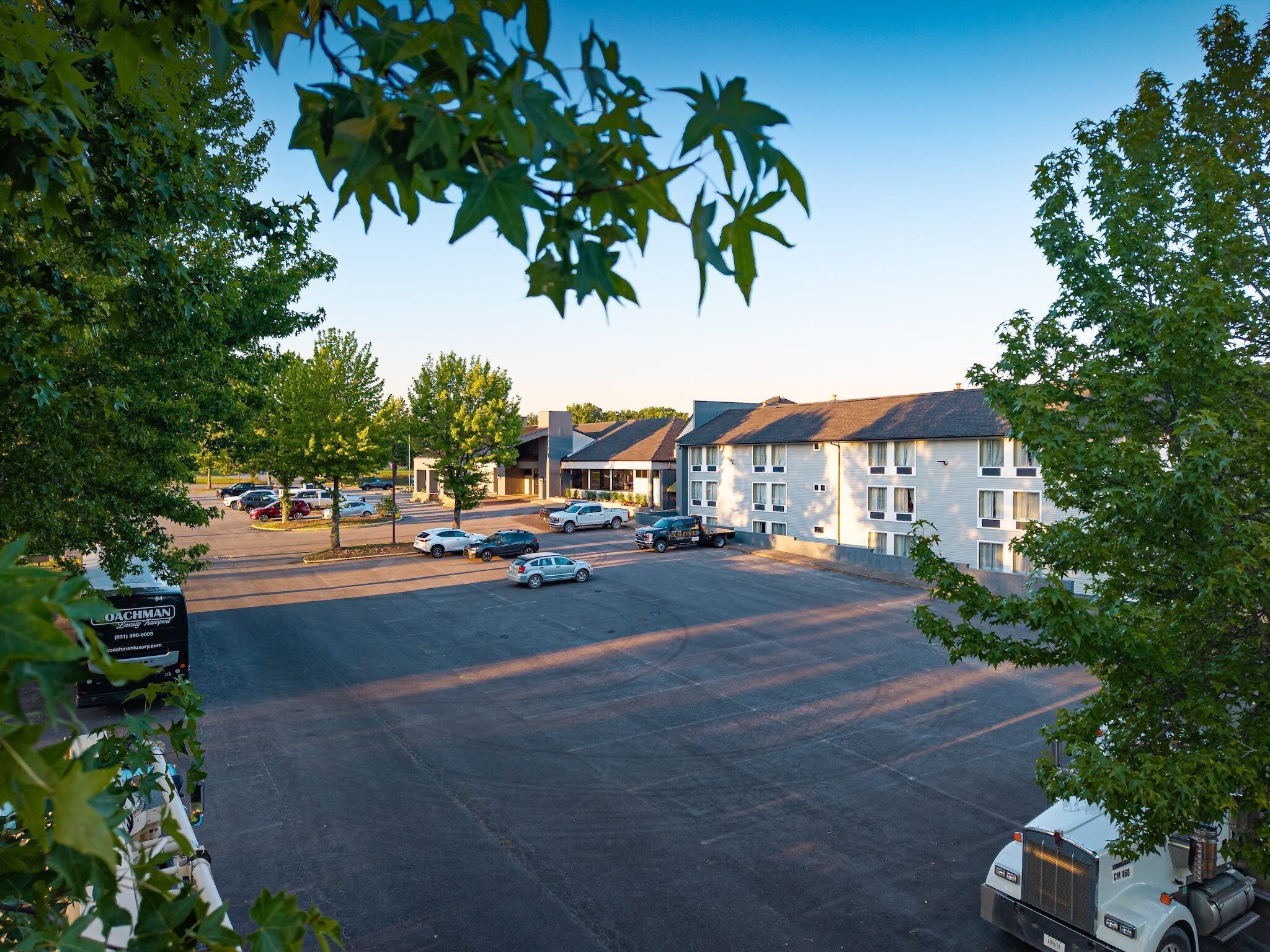 A parking lot with several cars and a truck, surrounded by trees and buildings with a flat roof.