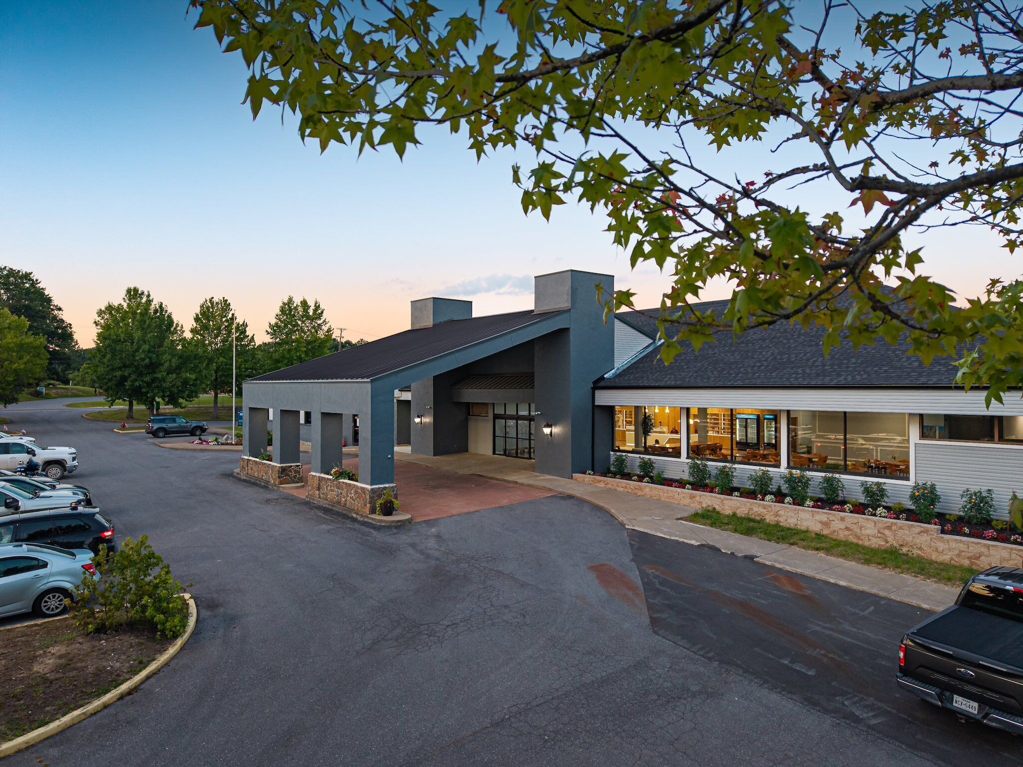 A modern building with a covered entrance, a parking lot, and a restaurant with outdoor seating.