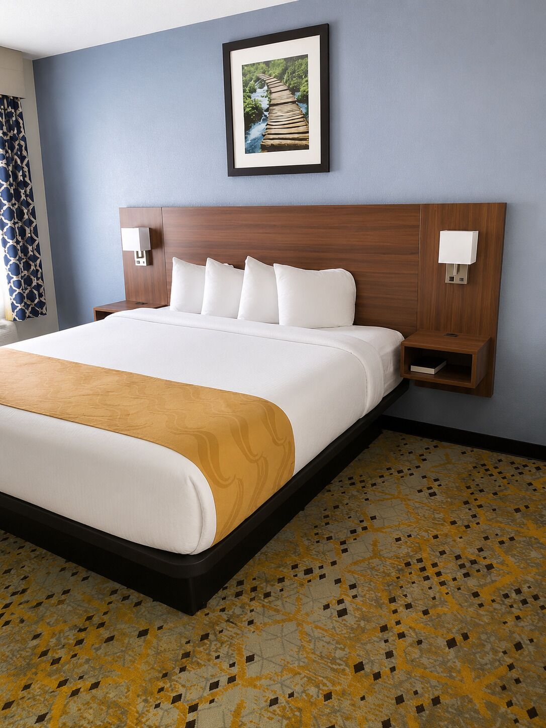 A hotel room with a large bed, a headboard, bedside tables, and a framed picture on the wall.