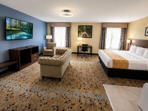 A hotel room with a bed, a sofa, a desk, and a TV. - Holiday Lodge Hotel & Conference Center (Oak Hill)