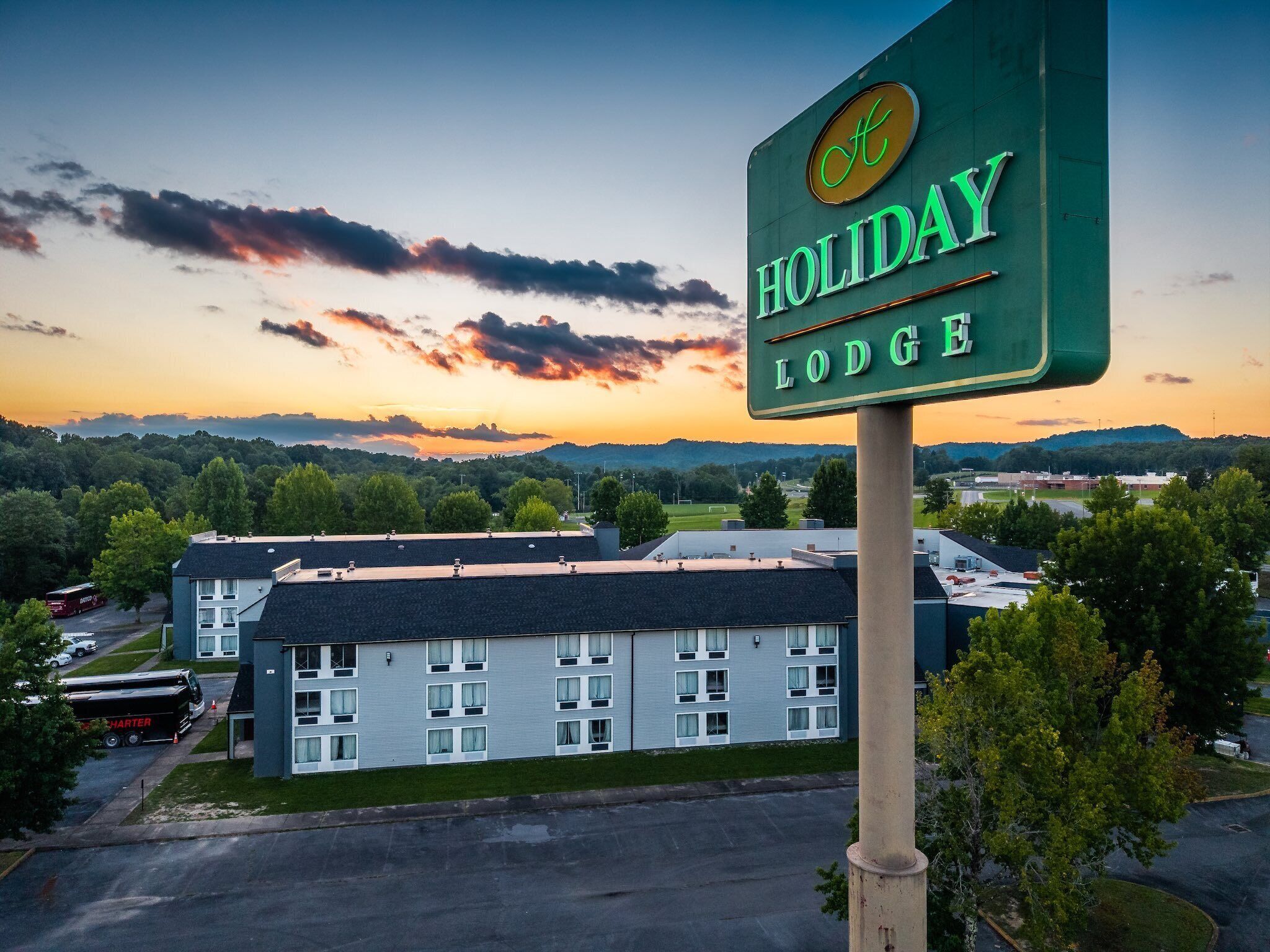 A Holiday Lodge sign with a view of a multi-story building and surrounding greenery.